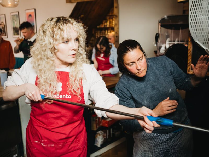 A woman wearing apron making pizza in a pizza oven. 
